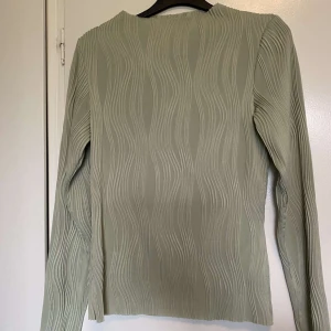 Olivgrön långärmad topp - Snygg olivgrön topp med lång ärm och ett unikt vågigt mönster. Perfekt för en stilren look. Passar bra till både jeans och kjol.