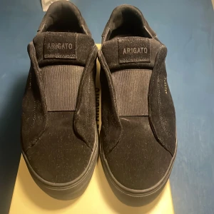 Svarta sneakers från Axel Arigato - Snygga svarta sneakers från Axel Arigato i mocka. De har en stilren design med elastiska paneler för enkel påtagning. Perfekta för en minimalistisk look. Använd 2 gånger!
