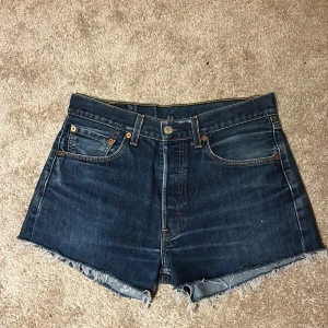 Jeansshorts från Levi's - Snygga mörkblå jeansshorts från Levi's med fransiga kanter och klassisk femficksdesign. Perfekta för en avslappnad stil. De har en knappgylf