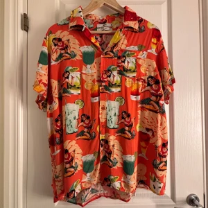 Färgglad kortärmad skjorta från Indigo - Säljer en färgglad kortärmad skjorta från Indigo med ett livligt mönster av drinkar och figurer. Skjortan har en avslappnad passform och knappar framtill. Perfekt för en somrig look! 🍹