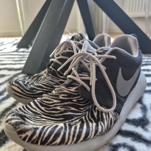 Nike Roshe Zebra (42) - Unika Nike sneakers med svart och vit zebramönstrad tå och mesh-ovandel. Snyggt grått swoosh på sidan och vita snören. Skorna har en rund tå och platt sula, perfekt för dig som vill sticka ut med djurprint. Materialet är syntet och textil.