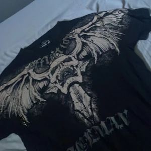 Affliction svart t-shirt med döskalle🦅 - Svart t-shirt från Affliction Signature Series, 100% bomull, med stor döskalle och vingar i grått och vitt på framsidan. Tryck med texten 'Affliction' och 'Iceman' fram, samt 'Affliction Chuck Liddell' bak. 