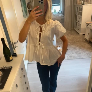 Vit blus med puffärm och knyt - Storlek: S-M❤️Superfin vit blus med puffiga korta ärmar och två knyt framtill som ger en söt och trendig look. Blusen har en volang nedtill och är gjord i mjukt bomullstyg. Perfekt för dig som gillar romantiska detaljer och vill ha en luftig topp. 