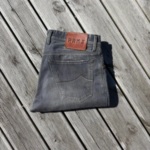 Grå jeans från Jacob Cohen PRMJ Limited edition - Snygga grå jeans från Jacob Cohen PRMJ med klassisk femficksdesign och bruna detaljer på knappar och läderpatch. Jeansen har raka ben och kontrastsömmar, tillverkade i mjukt bomullsmaterial. Perfekt för dig som gillar stilrena och tidlösa jeans. W31 