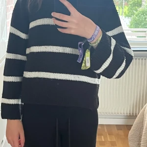 Svartvit randig stickad tröja Kappahl - Svart stickad tröja från Kappahl med breda vita ränder. Tröjan har en loose passform, långärmade ärmar och ribbade muddar. Perfekt för dig som gillar chill och enkel stil. Snygg att matcha med svarta jeans eller mjukisbyxor.