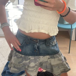 Jeanskjol med volanger och camomönster - Säljer en kort jeanskjol med cool volangkant i grått camouflagemönster. Kjolen har klassisk jeansmidja med fickor och bälteshällor, och den nedre delen är i mjukt tyg med två lager volanger. Perfekt för dig som gillar streetstyle och gillar Stockholm still💗💗