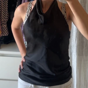 Svart satin linnetopp med draperad hals - Supersnygg svart linnetopp i satin med draperad halsringning och öppen rygg. Toppen är ärmlös och har en elegant, slät yta som ger en lyxig känsla. Aldrig använd, bra skick. Pris kan diskuteras 