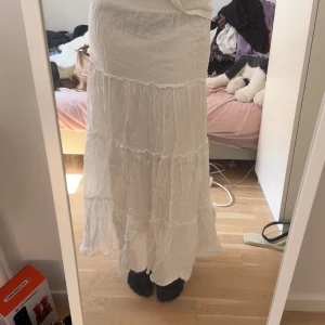 Vit långkjol med volanger  - Säljer en vit långkjol med flera lager volanger och skön, luftig känsl från venderbys. Kjolen har en bohemisk stil med rynkade sömmar och är perfekt för dig som gillar flowy vibes. Passar dig som vill ha en enkel men snygg kjol till sommaren.