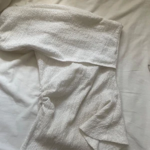 Vit över axeln topp med scrunch detaljer - Supersnygg vit axelbandslös topp med coolt rynkade detaljer på sidan. Materialet är strukturerat och känns mjukt mot huden, perfekt för dig som gillar en clean och fräsch look. Passformen är slim och klänningen har en modern vibe.