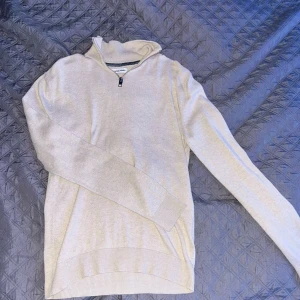 Beige stickad half zip-tröja - Snygg beige stickad tröja från Jack & Jones med half zip-dragkedja vid halsen. Tröjan har lång ärm och ribbade muddar, perfekt för lager-på-lager. Enkel och stilren design som funkar till många outfits passar både till S och Xs.