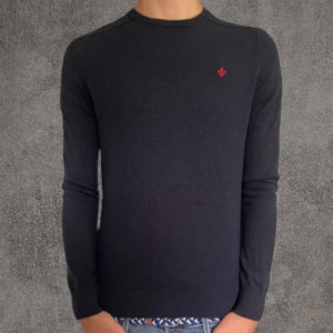 100% merinoull Mörkblå stickad tröja Morris - Snygg mörkblå stickad tröja från Morris i 100% merinoull. Tröjan har en klassisk rund hals och långärmade smala ärmar. På bröstet finns en liten röd broderad detalj som ger extra stilpoäng. Perfekt för dig som gillar enkel och clean look.