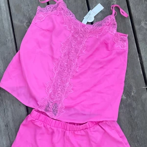 Risa pyjamas - Superfin rosa pyjamas från Lindex med tunna axelband och detaljerad spets längs halsringningen och framtill. Toppens material är mjukt och lätt, perfekt för varma dagar. Spetsen ger en extra touch av stil och gör toppen riktigt söt och trendig.