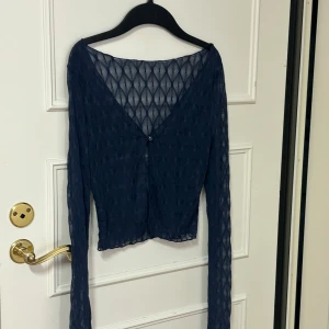 Mörkblå mesh kofta med knapp - Säljer en mörkblå mesh kofta med lång ärm och v-ringad hals. Koftan har ett transparent, geometriskt mönster och stängs med en liten knapp framtill. Perfekt att styla över ett linne eller topp för en cool layering-effekt. Säljer på grund av att den inte passar mig! Storlek är XS-S Använd 2 gånger💕