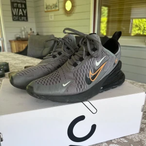 Nike 270 - Nike Air Max 270 sneakers i grått med svart och orange detaljer. Skorna är i skick 8/10 skulle jag säga, finns något litet hål men inget man tänker på vid användning. Box medföljer. Storlek 40 men sitter bra på mig som haft 41 i 270s hela tiden, men passar såklart 40 lika bra. (Priset kan sänkas lite vid snabb affär) oerhört bekväma!