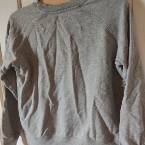 Grå tjocktröja - En simpel grå tjocktröja med hög urringning. Den ser skrynklig ut på bilden men den är av 100% bomull så den är inte skrylnlig vanligtvis.
