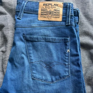 Replay Anbass blå jeans herr - Snygga Replay Anbass jeans i klassisk blå tvätt med diskreta slitningar. Modellen har fem fickor, dragkedja och knappstängning. Slim fit med smalare ben och normal midja. Ikonisk Replay-lapp baktill och broderad detalj på bakfickan. Perfekta för en chill och stilren look. Nästan oanvända, 9,5/10 skick. Width 33, lenght 34. Säljer för endast 499kr, nypris 1200