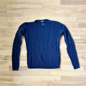 Mörkblå kabelstickad tröja Benetton - Snygg mörkblå kabelstickad tröja från United Colors of Benetton. Tröjan har rund hals, ribbade muddar och ett klassiskt kabelmönster över hela plagget. Perfekt för dig som gillar stilrena och tidlösa vibes. Långärmad och mjuk, passar till jeans eller chinos.