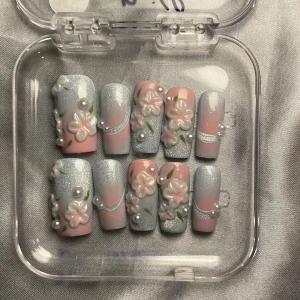 M - press ons med blommor och pärlor - Säljer ett set press-on naglar i pastellrosa och silverblå med glittereffekt. Naglarna har 3D-blommor, gröna blad och pärlor som dekoration. Formen är rak och mediumlång. Perfekt för dig som vill ha en söt och unik nageldesign.