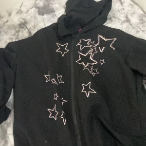 Svart hoodiejacka med stjärnor från SHEIN - Svart hoodiejacka från SHEIN med dragkedja och coola broderade stjärnor i vitt på framsidan. Jackan har huva och är långärmad, perfekt för dig som gillar en chill och trendig stil. Passar dig som vill sticka ut med snygga detaljer.