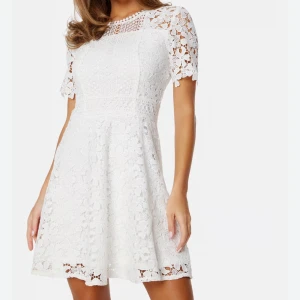 Vit spetsklänning / studentklänning - Superfin vit kortklänning med blommig spets och rund hals. Klänningen har korta ärmar och ett figurnära liv med markerad midja. Perfekt för student