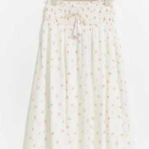 Vit ginatricot maxi skirt- med ett Ros mönster  - Superfin vit långkjol med små rosa rosor och smock i midjan. Kjolen har en söt snörning framtill och är gjord i ett lätt och luftigt bomullstyg. Perfekt för varma dagar när du vill känna dig både söt och bekväm. Originellt pris:300 kr 