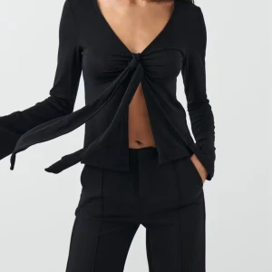 Slutsåld Svart långärmad omlottopp med knyt - Snygg svart omlottopp med lång ärm och djup v-ringning. Toppen har ett coolt knyt framtill som ger en öppen look över magen. Perfekt för dig som gillar trendiga och stilrena plagg med lite edge. Passar till både jeans och kostymbyxor. Använd två gånger