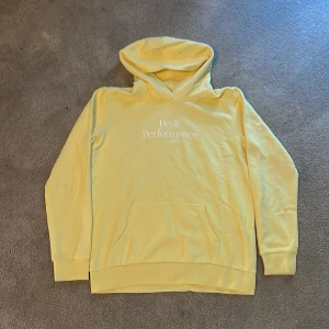 Gul t-shirt och hoodie från Peak Performance - Fräsch gul t-shirt och hoodie från Peak Performance med vit logga tryckt på bröstet. Klassisk rund hals och korta ärmar, perfekt för dig som gillar stilren och sportig vibe. Mjuk bomull som känns skön mot huden och passar till jeans eller shorts.