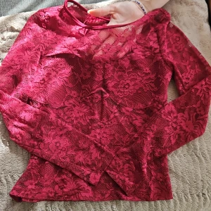 Vinröd spetsblus med blommönster - Säljer en vinröd långärmad blus i genombruten spets med blommigt mönster. 