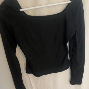 Svart ribbad topp från SHEIN - Svart långärmad topp från SHEIN i storlek S. Toppen har en bred, fyrkantig urringning och är tillverkad i mjuk bomull och polyester. Ribbad struktur med diskreta vertikala ränder ger en clean och stilren vibe. 