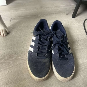 Adidas Busenitz sneakers marinblå - Säljer ett par Adidas Busenitz sneakers i marinblå mocka med klassiska vita ränder på sidorna och vit häl. Skorna har snörning och en platt gummisula med hexagonmönster undertill. Perfekt för dig som gillar streetstyle och skate. Storlek 44 knappt använda