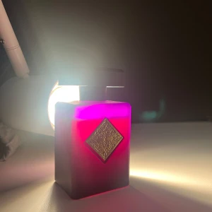 Initio Side Effect 90 ml - Initio Side Effect parfym i en lyxig, fyrkantig flaska med djup lila och röd ton. Flaskan har en dekorativ guldfärgad metallplatta framtill och ett svart lock. Perfekt för dig som gillar exklusiva och unika dofter. Cirka 80 ml kvar