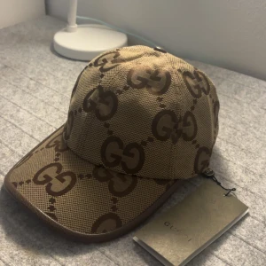 Beige Gucci keps - Skriv dm för video. Storlek ”M”. Säljer en snygg beige keps från Gucci med det klassiska GG-logomönstret i mörkbrunt över hela kepsen. Kepsen har böjd skärm och justerbart band bak i brunt läder. Materialet är slitstark canvas och detaljerna är riktigt lyxiga. 