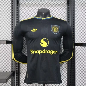 Manchester United svart långärmad tröja - Snygg svart Manchester United fotbollströja från Adidas med lång ärm och gula detaljer. Tröjan har klubbmärke på bröstet, Snapdragon-logga och gula ränder längs ärmarna. Kragen har blå och gula inslag. Materialet är lätt och andas, perfekt för match eller träning.