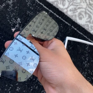 Louis Vuitton svarta monogram solglasögon - Säljer ett par svarta Louis Vuitton solglasögon med spegelglas och ikoniskt LV-monogram över hela linsen. Modellen är Z1082E och har en modern, kantig form med breda skalmar där Louis Vuitton är ingraverat. Riktigt statement piece för dig som gillar lyxig streetstyle.