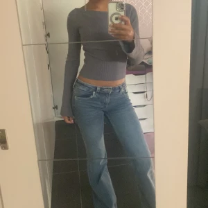 Grå ribbad topp från Divided - Säljer en grå ribbad långärmad topp från Divided. Modellen är croppad med utsvängda ärmar och har en snygg, vid urringning. Perfekt att styla med jeans eller kjol för en chill look.