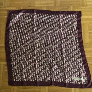 Lila Dior halsduk i siden - Snygg lila halsduk från Christian Dior i glansigt sidenmaterial. Halsduken har ett ikoniskt mönster med Dior-loggan över hela ytan och en bredare enfärgad kant runtom. Perfekt accessoar för att lyfta din outfit.