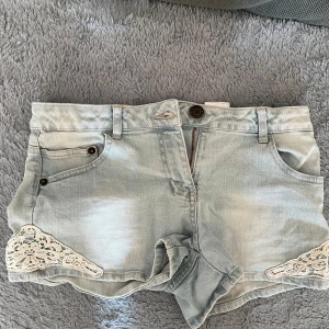 Ljusblå jeansshorts med spets från Pepperts - Snygga ljusblå jeansshorts från Pepperts med coola spetsdetaljer i vitt på sidorna. Klassisk femficksmodell, bälteshällor och uppvikta benslut. Perfekta för varma dagar när du vill ha en chill och trendig look.