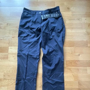 Marinblå golfbyxor från Abacus - Snygga marinblå golfbyxor från Abacus i klassisk rak modell. Byxorna har hällor för bälte, fickor fram och bak samt stängs med knapp och dragkedja. Perfekta för en clean och stilren look. Materialet känns lätt och smidigt.