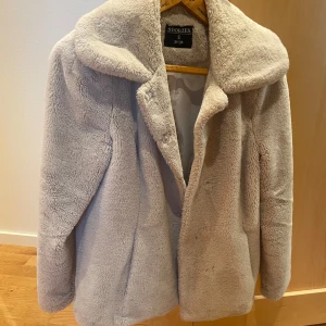 Beige teddyjacka från & Other Stories - Supermjuk och fluffig teddyjacka i beige från & Other Stories. Jackan har bred krage, rak passform och är helfodrad. Perfekt för kalla dagar när du vill vara både varm och snygg. Stängs med dolda knappar framtill.