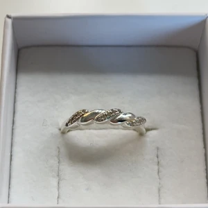 Flätad silverring med stenar - Snygg ring i silverfärg med flätad design och små glittrande stenar infällda i bandet. Perfekt för dig som gillar stilrena smycken med en liten twist. Ringen levereras i en vit ask.
