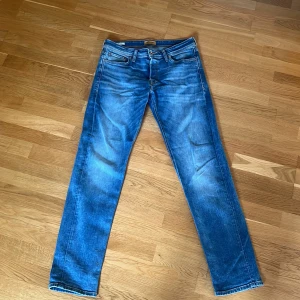 Blå tapered jeans Tapered/Mike 30/34 - Snygga blå jeans i modellen Tapered/Mike med avsmalnande ben och klassisk femficksdesign. Jeansen har en schysst tvätt med slitningar och kontrastsömmar. Perfekta för dig som gillar en modern och avslappnad look. Passar folk mellan 170-180.