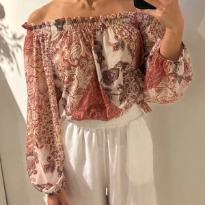 Mönstrad offshoulder blus Gina Tricot - Supersöt offshoulder blus från Gina Tricot i storlek XS. Blusen har ett paisleyinspirerat mönster i rostbrunt, beige och inslag av svart. Långa puffiga ärmar med resår och smockad nederkant. Tunn och luftig polyester, perfekt för vår och sommar.