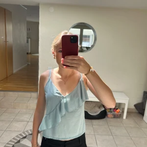 Ljusblå linnetopp med volang H&M XS - Supersöt ljusblå linnetopp från H&M i storlek XS. Toppen har smala axelband, v-ringning och en snygg volangdetalj framtill. Perfekt för varma dagar och enkel att styla med jeans eller kjol.