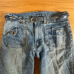 Blå bootcut jeans med coola detaljer  - Ljusblå jeans med slitningar och detaljer. Dessa köpte ja secondhand! De har ingen knapp kvar men dragkedja finns (se sista bilden) Och det funkar utmärkt att ha ett skärp till (vilket jag kommer skicka med också)    Midjemått =W25  innebenslängd= 80
