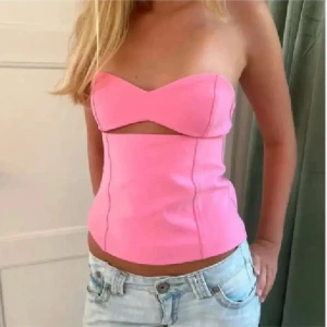 Rosa off shoulder topp - Säljer en snygg rosa korsett-topp med axelbandslös design och cool cut out-detalj under bysten. Toppen är croppad och har en figurnära passform som framhäver midjan. Perfekt att styla med jeans för en trendig look.