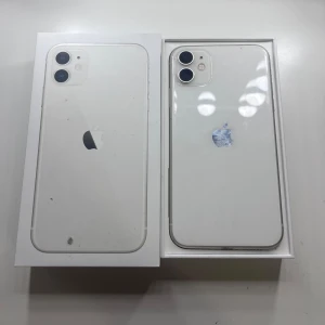 Iphone 11 - Bilderna visar en vit iPhone 11 med originalkartong och ett svart skal. Telefonen har dubbla kameror på baksidan och ser ut att vara i nytt skick. Perfekt för dig som vill ha en snygg och pålitlig smartphone till ett bra pris. Allting är i nyskick förutom batteri som ligger lite lägre! 128GB och mobilskal tillkommer! Olåst.