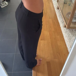 Svarta kostymbyxor med raka ben - Snygga svarta kostymbyxor med raka, lite loose ben och klassiska fickor. Byxorna har hällor för bälte och stängs med dragkedja och knapp. Perfekta för en clean och stilren look, passar till både sneakers och boots. Innerbenslängd: 75cm Midjemått: 38cm 