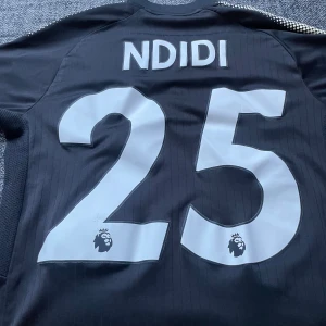 Leicester City Ndidi #25 svart matchtröja - Snygg svart Leicester City fotbollströja från Puma med Ndidi och nummer 25 på ryggen. Tröjan har klubbmärke och King Power-logga i guld framtill, samt Premier League-logga på siffrorna. Tillverkad i lätt och ventilerande material, perfekt för match eller träning.