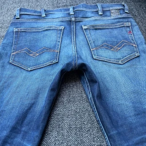 Replay Jondrill jeans blå, stl 28 - Säljer ett par snygga Replay Jondrill jeans i klassisk blå tvätt. Jeansen har raka ben, normal passform och coola detaljer på bakfickorna. Märket syns tydligt på fickan och insidan. Perfekta för dig som gillar stilrena och bekväma jeans.