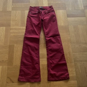 Vinröda bootcut byxor  - Snygga vinröda byxor från Coretnox med bootcut passform. Klassisk femficksmodell med silverfärgade nitar och knapp. Byxorna är tillverkade i ett mjukt bomullstyg och har normal midja. Perfekta för dig som vill sticka ut med färg.